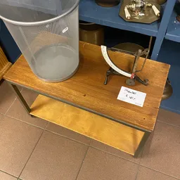 Houten tafel met zwarte metalen poten met daarop een grijze wasmand, glazen vazen en een prijskaartje van 6,50 euro