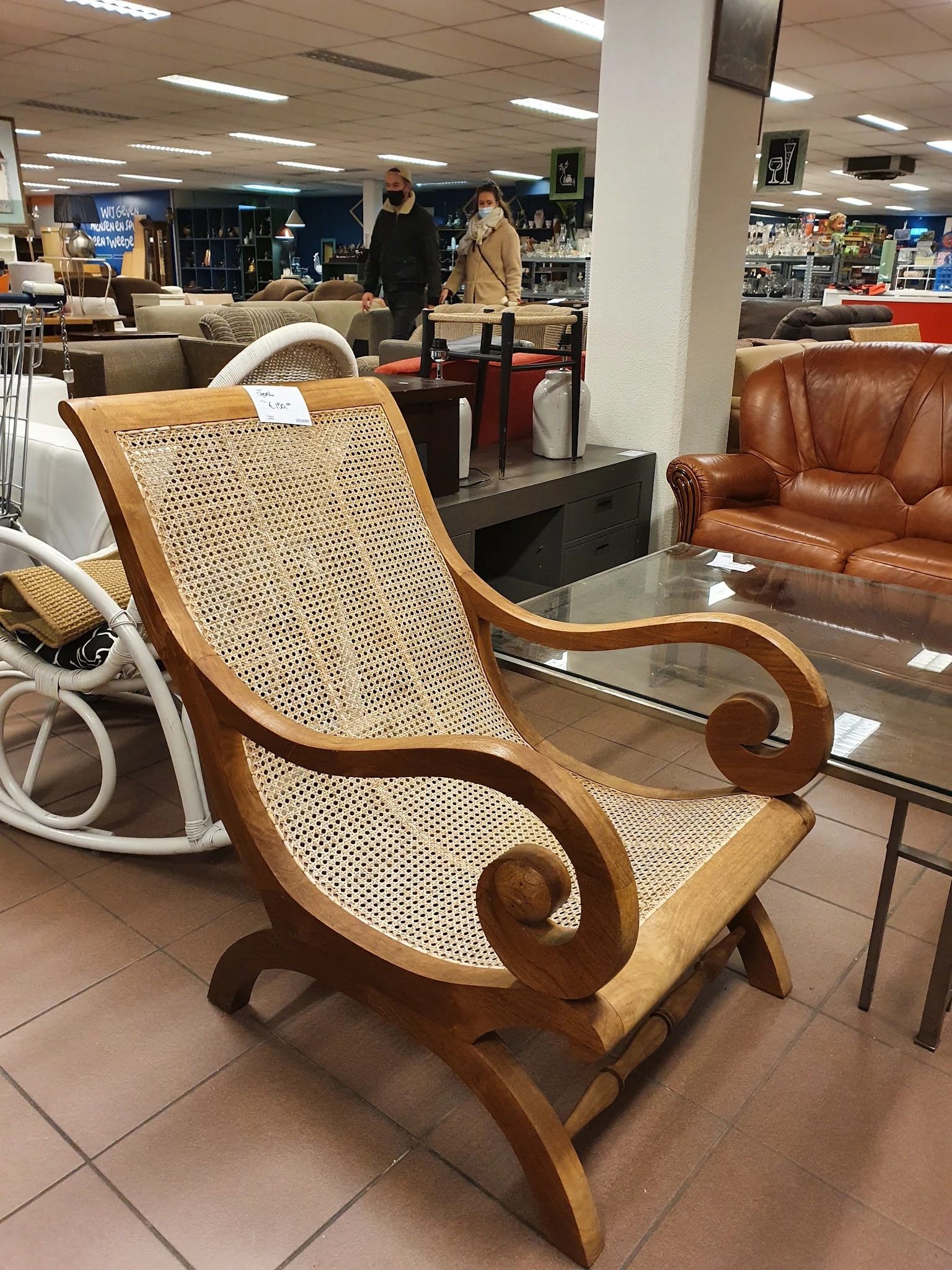 Houten fauteuil met rieten rugleuning en gesculpteerde armleuningen in een kringloopwinkel