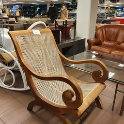 Houten fauteuil met rieten rugleuning en gesculpteerde armleuningen in een kringloopwinkel