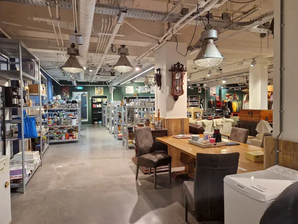Winkelinterieur met houten meubels, bruine stoelen, houten tafel, stellingen en diverse spullen in de kringloopwinkel