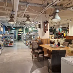 Winkelinterieur met houten meubels, bruine stoelen, houten tafel, stellingen en diverse spullen in de kringloopwinkel