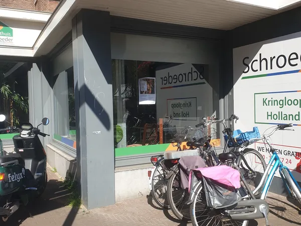 Voorkant van kringloopwinkel met vitrine, fietsen geparkeerd ervoor en winkelnaam gedeeltelijk zichtbaar