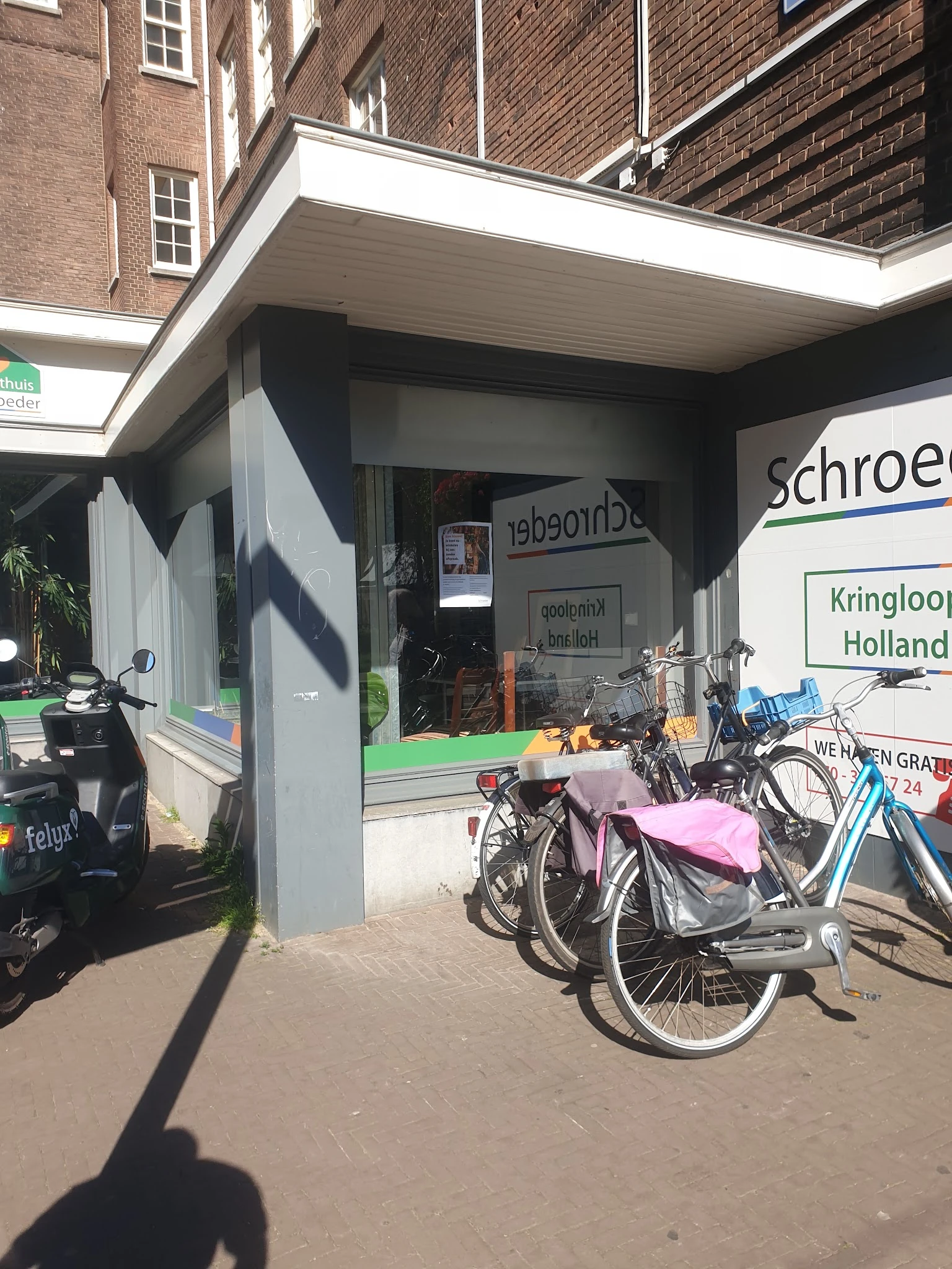 Voorkant van kringloopwinkel met vitrine, fietsen geparkeerd ervoor en winkelnaam gedeeltelijk zichtbaar