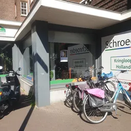 Voorkant van kringloopwinkel met vitrine, fietsen geparkeerd ervoor en winkelnaam gedeeltelijk zichtbaar