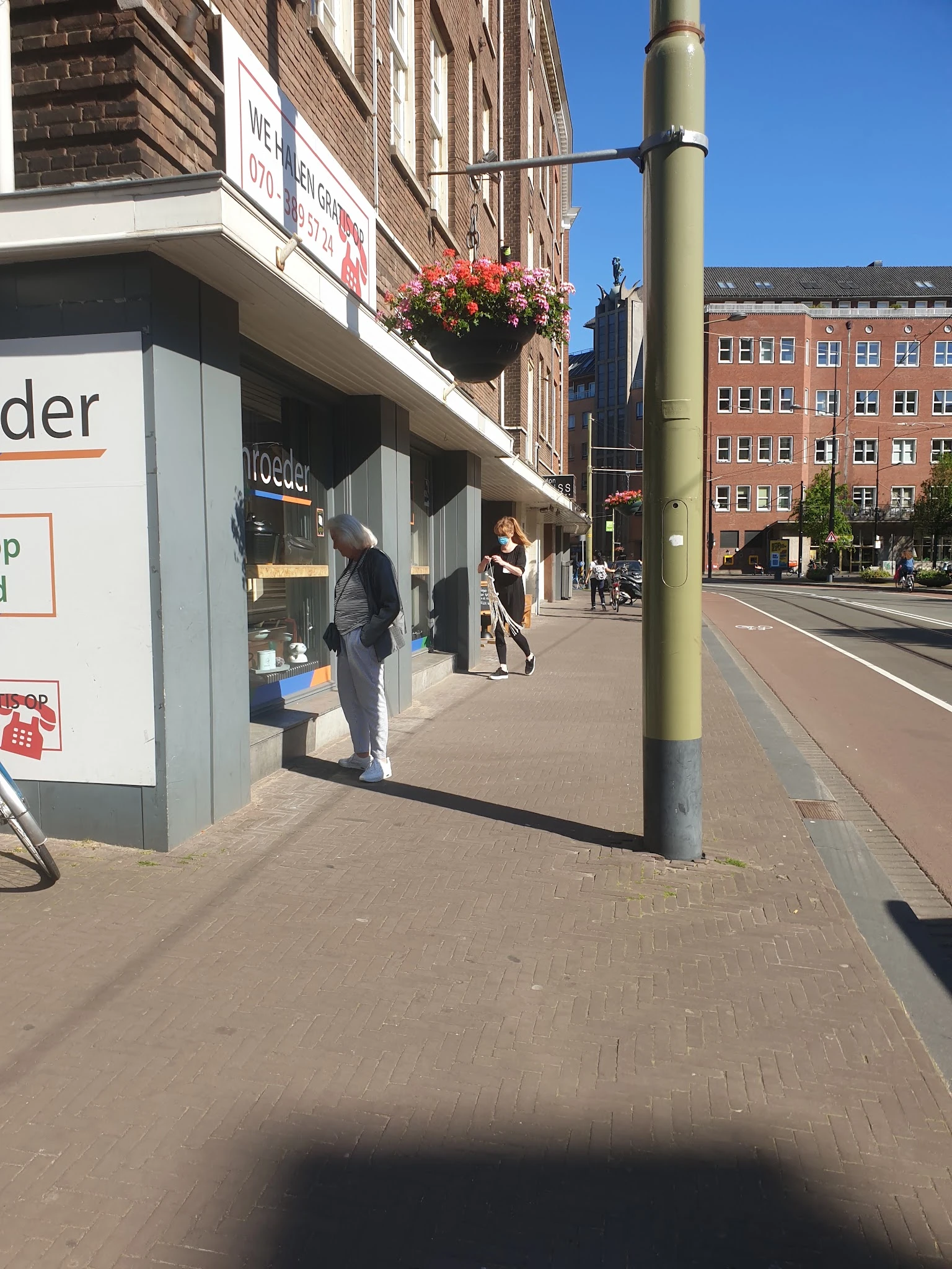 Straatgevel van kringloopwinkel met etalageruit, deel van winkelnaam zichtbaar, personen op straat