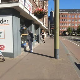 Straatgevel van kringloopwinkel met etalageruit, deel van winkelnaam zichtbaar, personen op straat