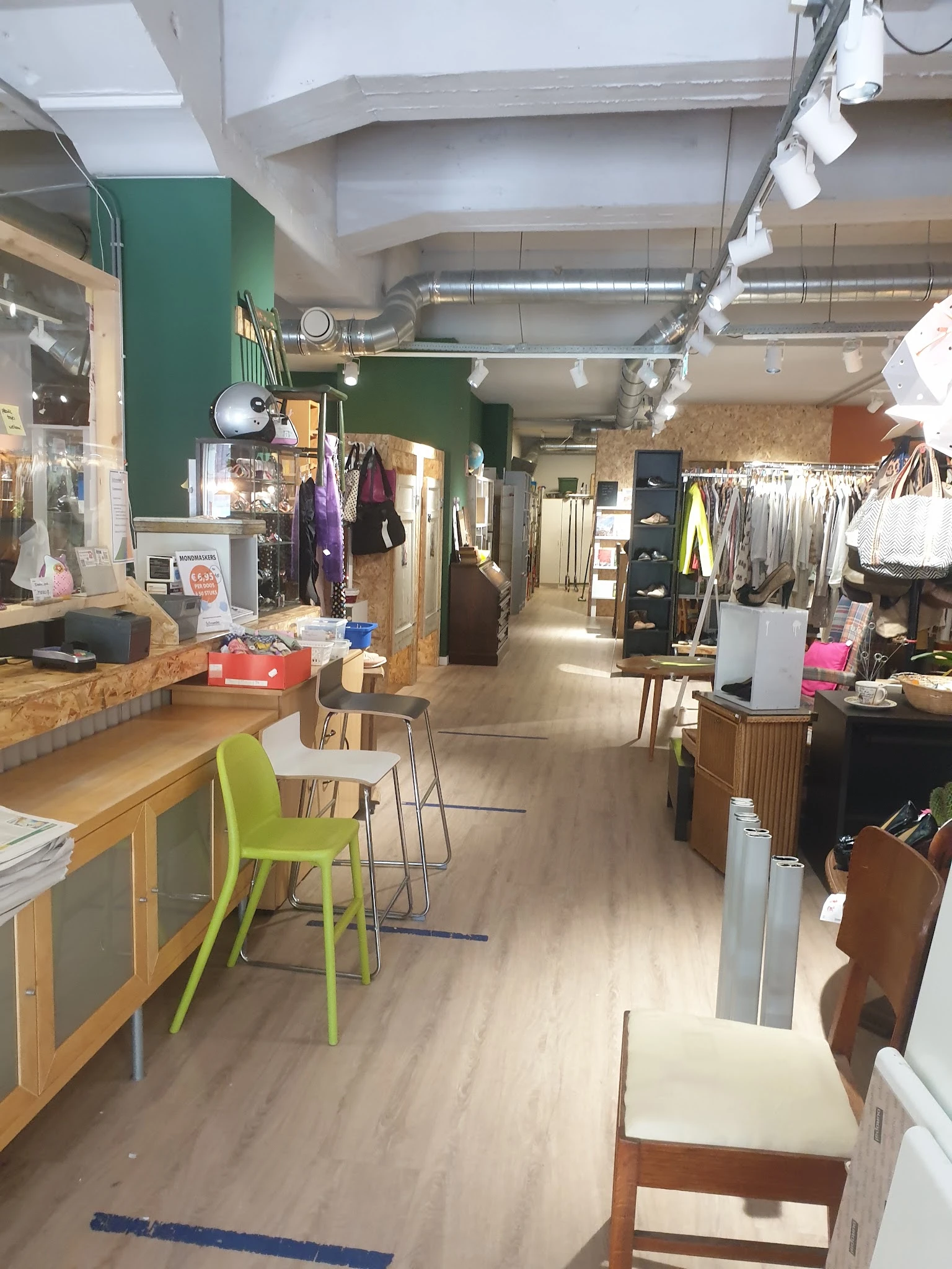 Winkelvloer van kringloopwinkel met rekken met kleding, houten toonbank met groene stoel, groene muur op achtergrond