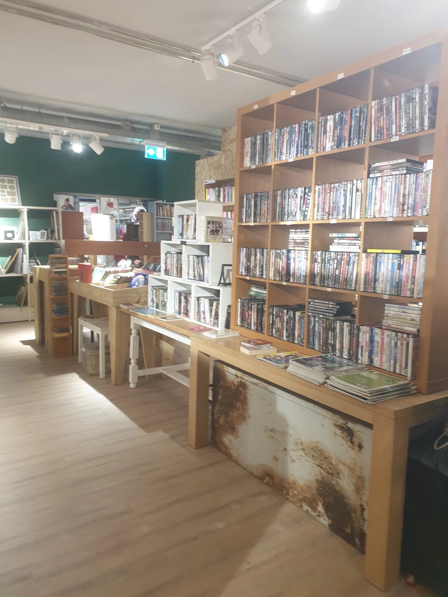 Winkelinterieur met houten tafels, houten rekken vol dvd's en boeken tegen de wanden, groene muur op de achtergrond