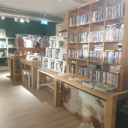 Winkelinterieur met houten tafels, houten rekken vol dvd's en boeken tegen de wanden, groene muur op de achtergrond