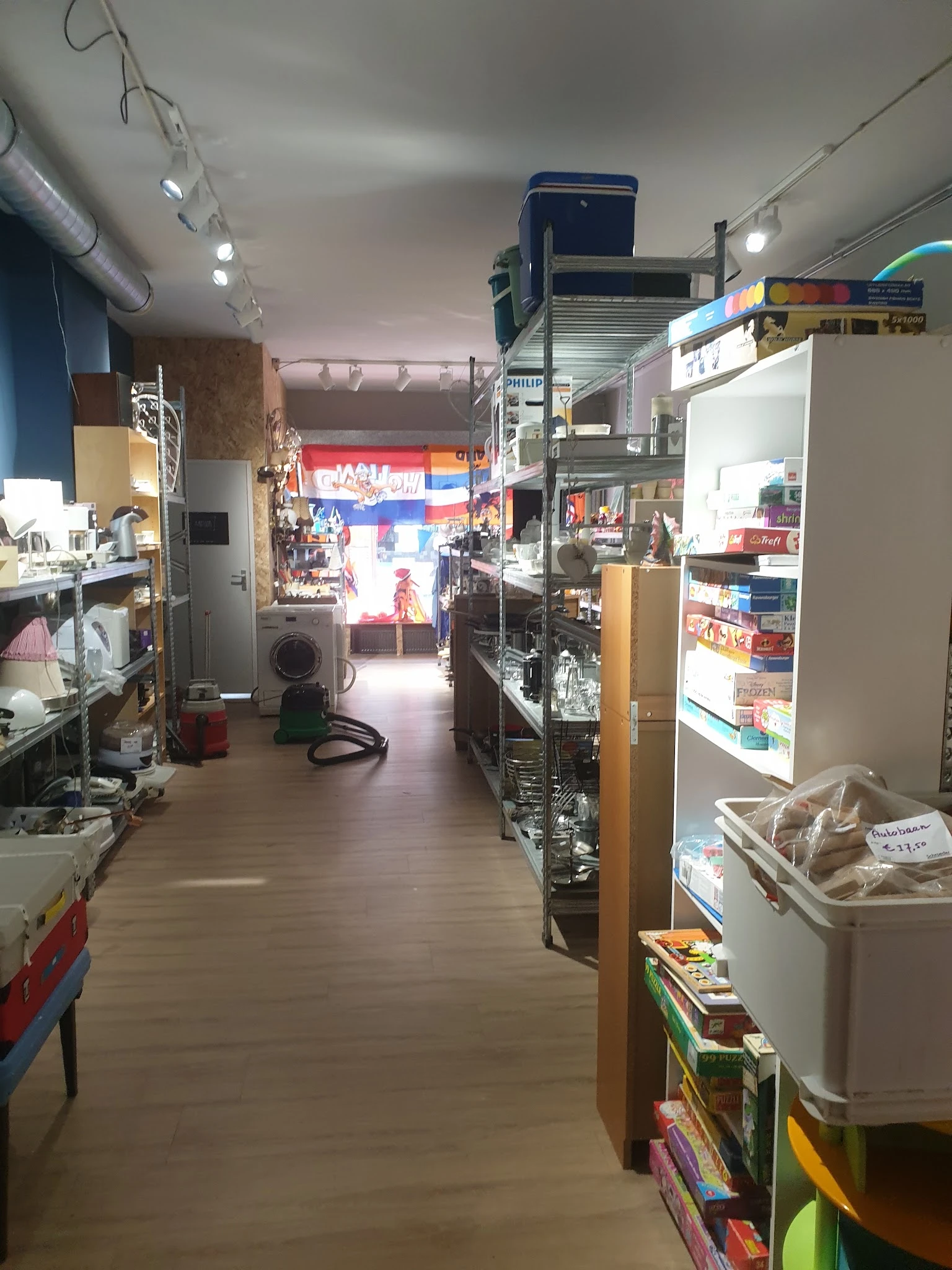 Winkelinterieur van kringloopwinkel met stellingen, schappen en diverse tweedehands artikelen langs de wanden
