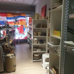 Winkelbinnenruimte met stellingen vol huishoudwaren, manden en servies, zicht op winkelpad naar achteruitgang