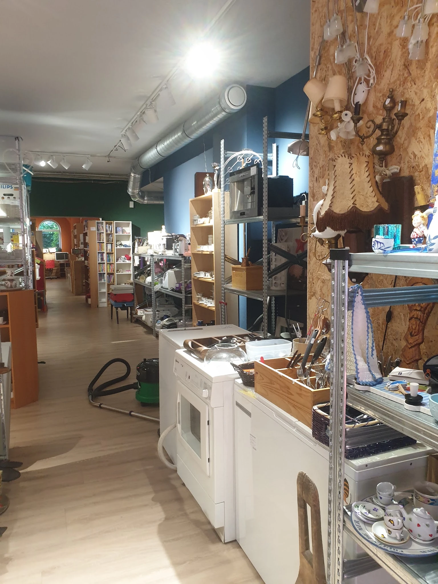 Winkelvloer van kringloopwinkel met stellingen, werkbank en diverse gebruiksartikelen