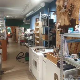 Winkelvloer van kringloopwinkel met stellingen, werkbank en diverse gebruiksartikelen