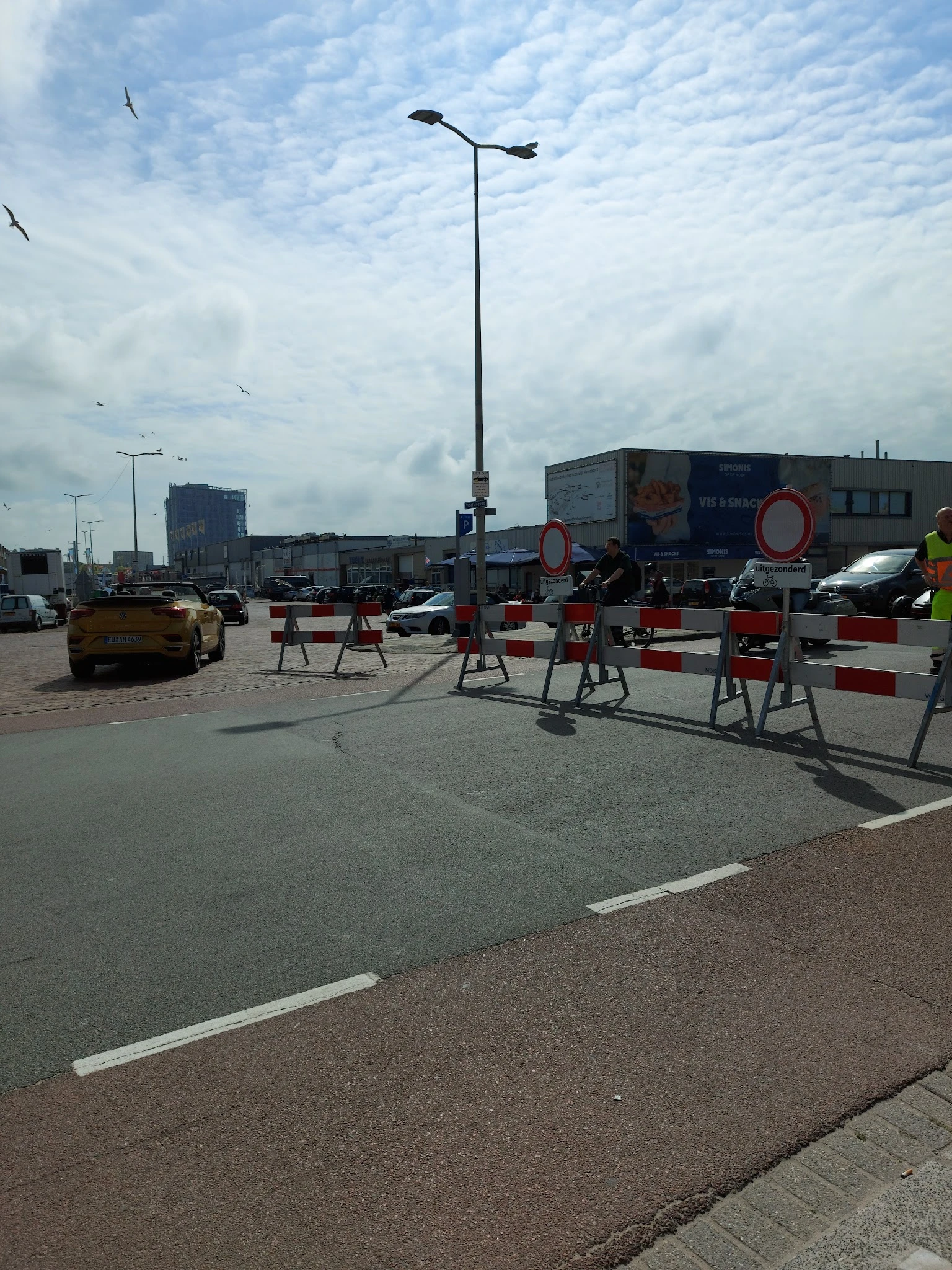 Parkeerterrein met afzetting en bouwverkeer, winkelgebouwen op achtergrond