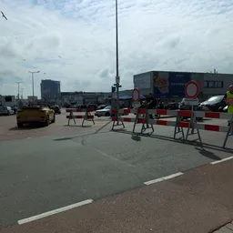 Parkeerterrein met afzetting en bouwverkeer, winkelgebouwen op achtergrond