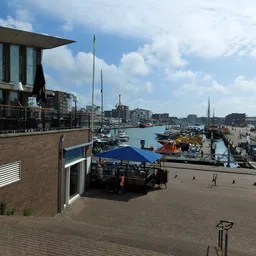 Uitzicht op haven met boten, een modern gebouw links en een blauwe markering op de kade