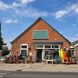 Voorgevel van kringloopwinkel Second Life Brocante, een rood bakstenen gebouw met groene raamluiken en uitgestalde spullen.