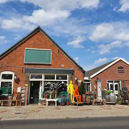 Rode bakstenen kringloopwinkel met groene ramen, uitgestalde spullen op het terras en bij de ingang