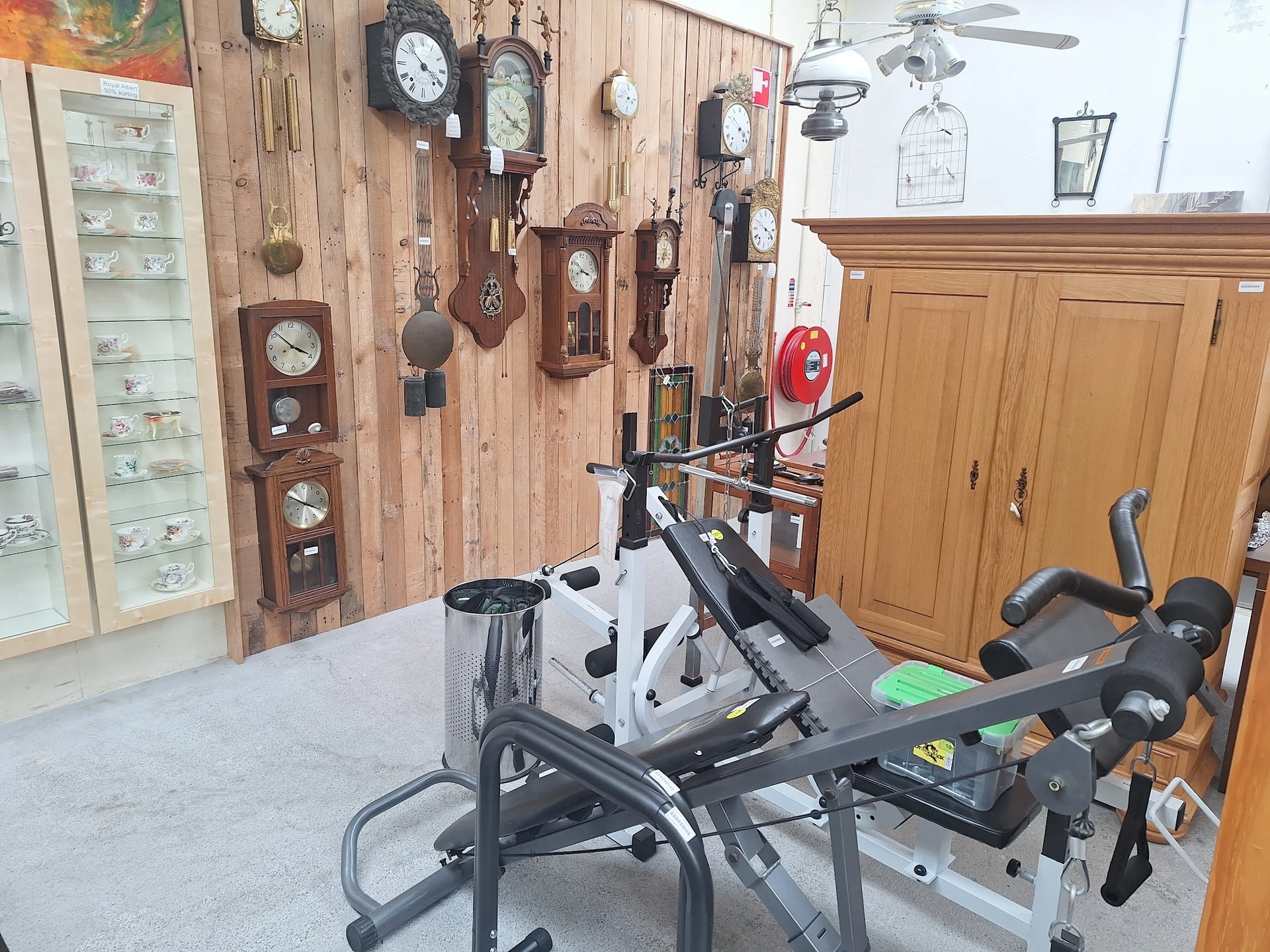 Winkelbinnenruimte met aan muur bevestigde klokken, fitnessapparatuur en houten kasten