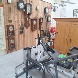 Winkelbinnenruimte met aan muur bevestigde klokken, fitnessapparatuur en houten kasten
