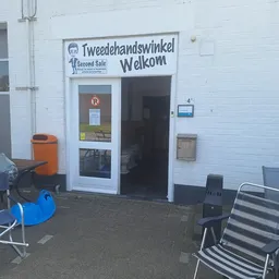 Witte gevel van Tweedehandswinkel Welkom met ingang, uithangbord en terras met stoelen