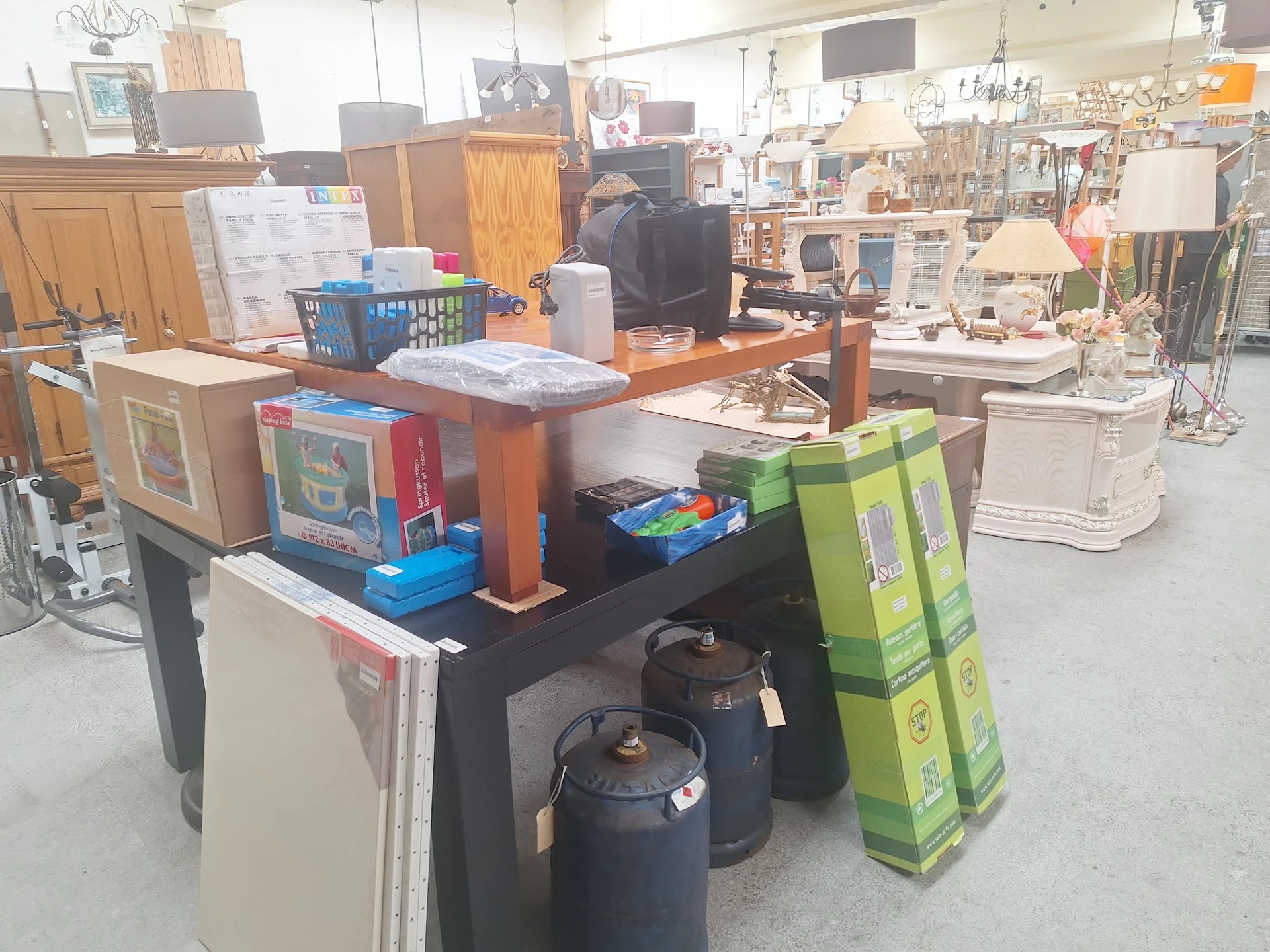 Winkelvloer met diverse huishoudelijke items, meubels en dozen op en rond een tafel