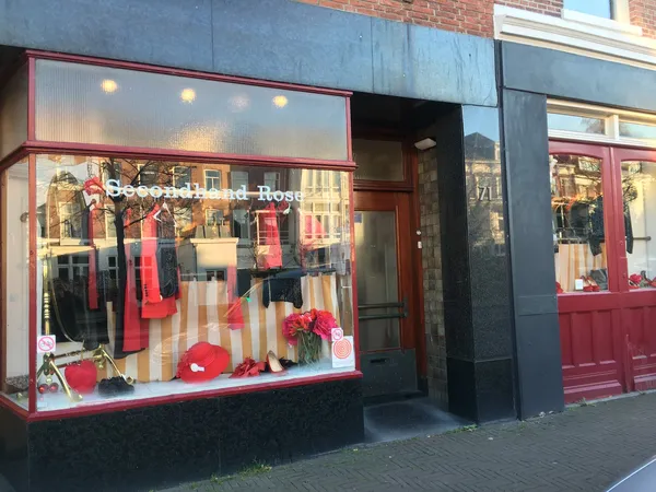 Winkelgevel met rood-wit interieur, etalage met rode kleding en decoraties, winkelnaam boven deur