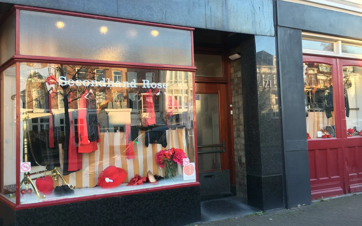Gevel van Secondhand Rose met rood-zwarte pui en etalage vol tweedehands kleding en accessoires
