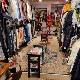 Winkelvloer met kledingrekken aan beide zijden en display-tafels in het midden, gevuld met tweedehands kleding en accessoires