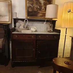 Antieke donkerhouten commode met marmeren blad en wit porselein servies erop