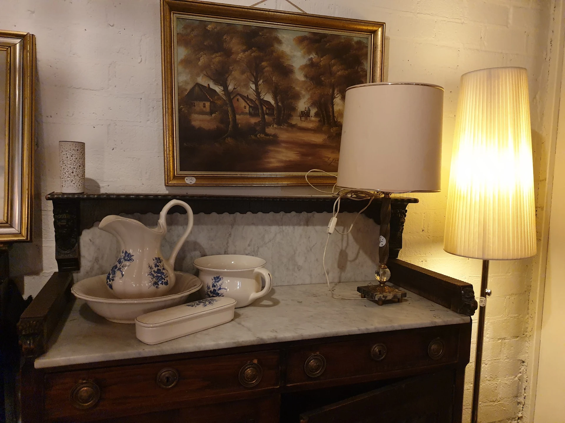 Antieke donkerhouten wastafel met marmeren blad, decoratieve kan en kom met blauwe details, en verlichte staande lamp