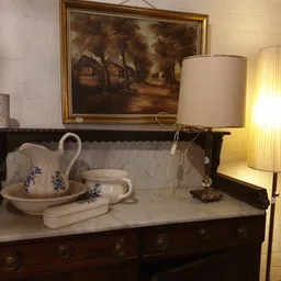 Antieke donkerhouten wastafel met marmeren blad, decoratieve kan en kom met blauwe details, en verlichte staande lamp