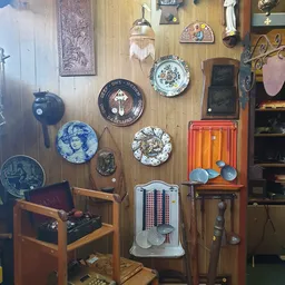 Verzameling tweedehands huisraad aan muur: decoratieve borden, vintage radio, stoelen, spiegel en diverse antieke voorwerpen