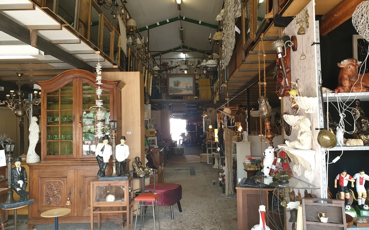 Interieur van kringloopwinkel met houten meubels, decoratieve objecten en diverse spullen langs beide zijden van een gangpad
