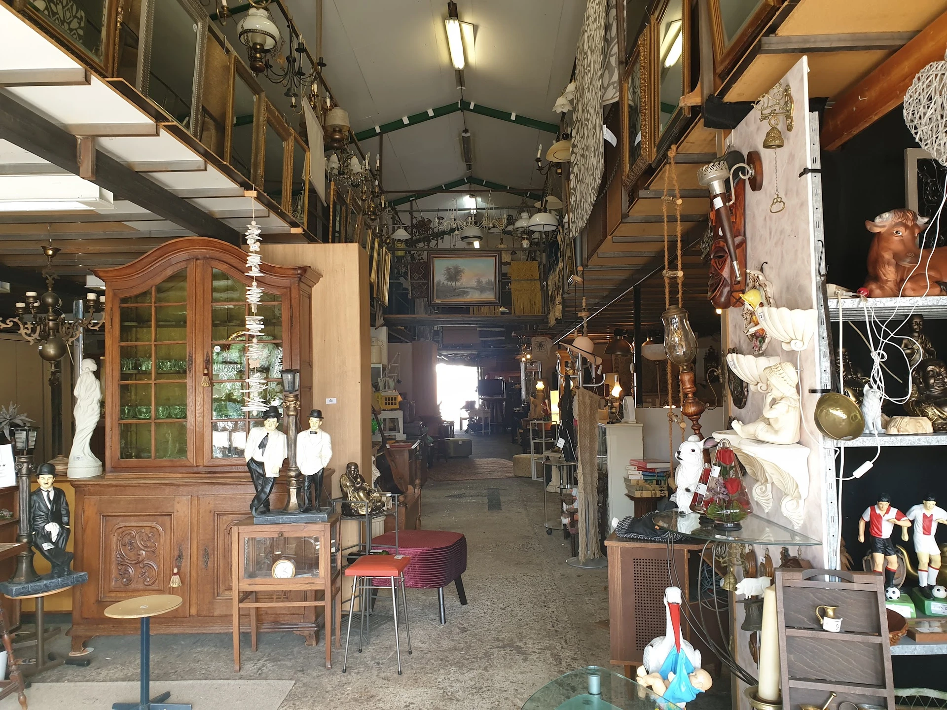 Interieur van kringloopwinkel met houten meubels, decoratieve objecten en diverse spullen langs beide zijden van een gangpad