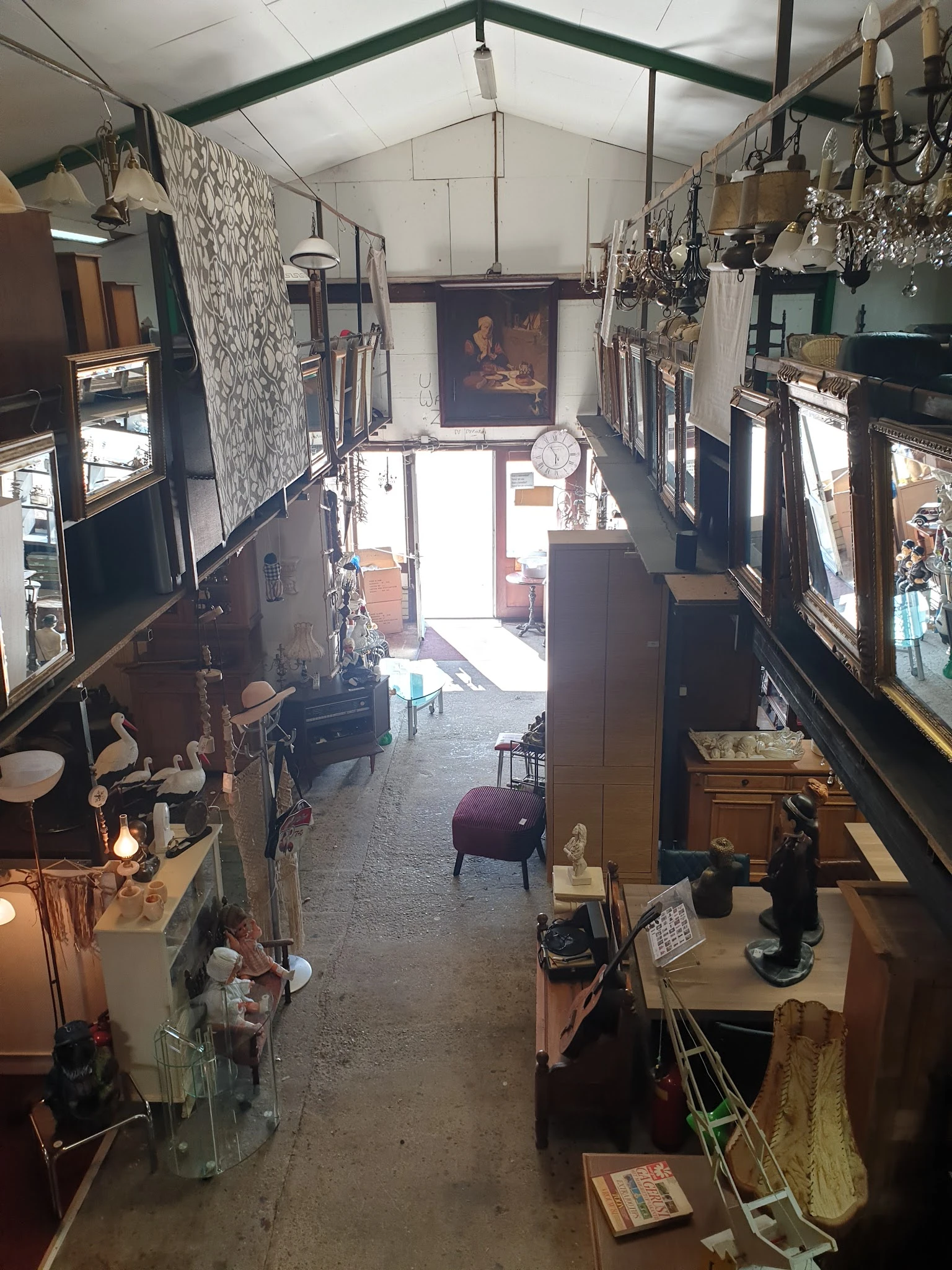 Winkelvloer van kringloopwinkel met diverse meubels, decoratie en spullen aan beide zijden, zicht op ingang vooraan