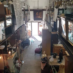Winkelvloer van kringloopwinkel met diverse meubels, decoratie en spullen aan beide zijden, zicht op ingang vooraan