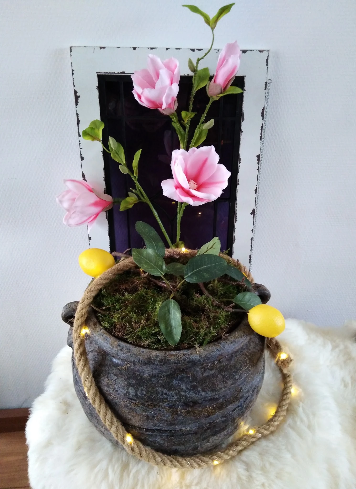 Potplant met roze bloemen, geel fruit en touw, tegen donkere achtergrond
