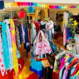 Kleurrijke winkelinterieur met kledingrekken, hangertjes in regenboogkleuren en decoratieve elementen aan het plafond