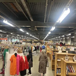 Overzicht van de winkelvloer met kledingrekken, stellingen met boeken en huishoudartikelen, en bezoekers die rondkijken