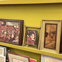 Drie ingelijste schilderijen en kunstwerken tegen gele muur op een plank