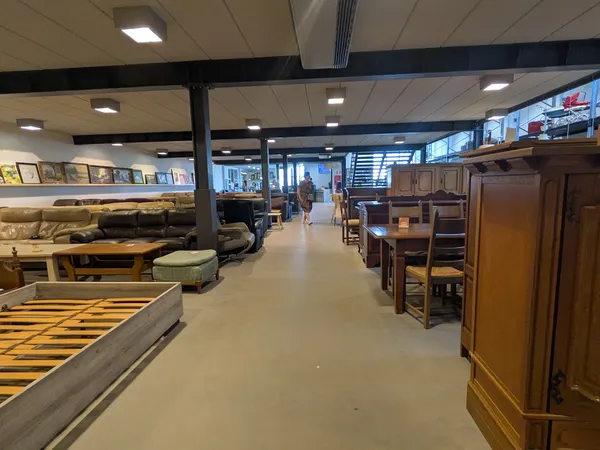 Ruim winkelinterieur met meubels, bedden en kasten uitgestald langs beide zijden van het middenpad