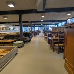 Ruim winkelinterieur met meubels, bedden en kasten uitgestald langs beide zijden van het middenpad