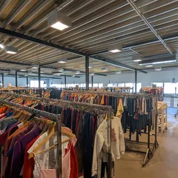 Rekken met tweedehands kleding in verschillende kleuren en stijlen in een grote winkelruimte
