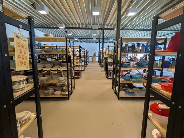 Lange winkelgang met zwarte stellingen vol serviesgoed en huishoudartikelen langs beide zijden