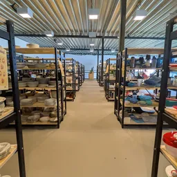 Lange winkelgang met zwarte stellingen vol serviesgoed en huishoudartikelen langs beide zijden