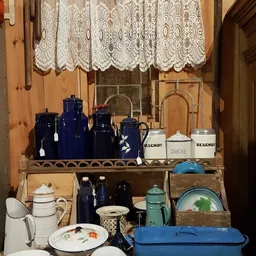 Kastplank met antieke huishoudartikelen: blauwe porseleinen potjes, witte suikerpot, groene theepot en servies