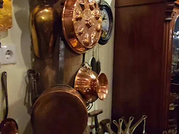 Koperen en bronzen keukengerei en decoratieve items opgehangen aan de wand, inclusief pannen, scheplepels en een wandklok