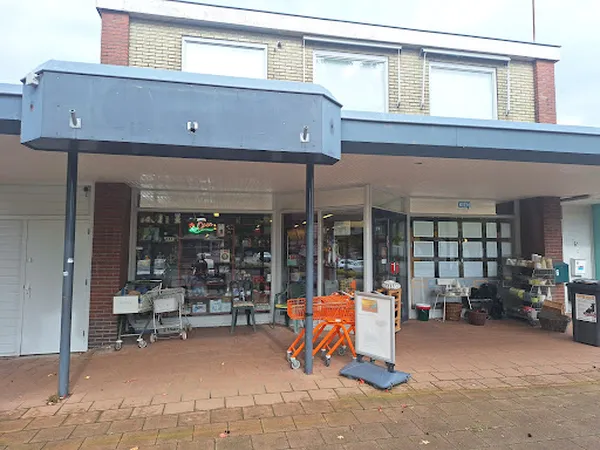 Winkelpui van kringloopwinkel met bruine bakstenen gevel, grote raampartijen, blauwe afdakking en oranje bouwmaterialen op he