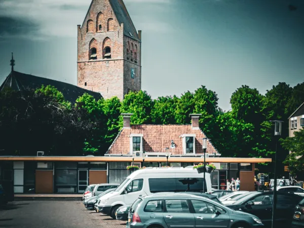 Voorgevel van winkel met rode bakstenen dak, kerkflat op achtergrond en geparkeerde auto's op het plein